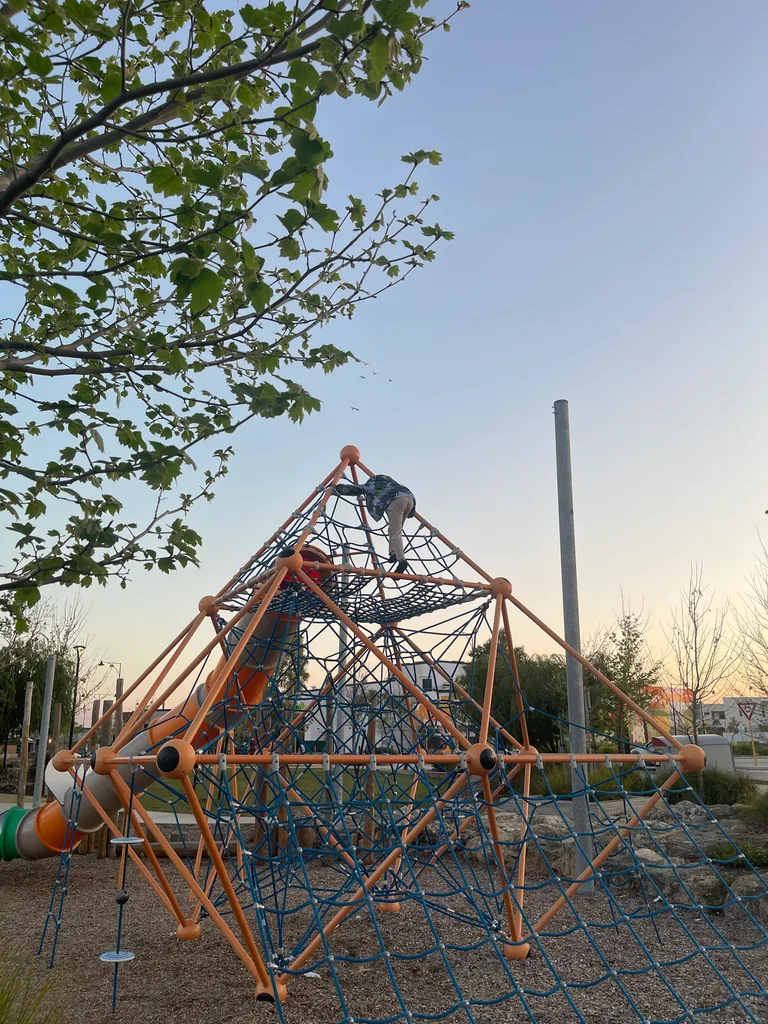 An AKademy38 student climbing a rope pyramid at a local playground at dusk