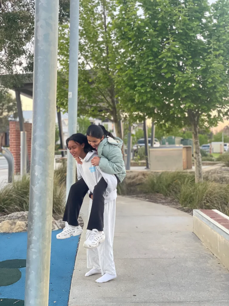 Two AKademy38 students laughing together outdoors, one giving the other a piggyback